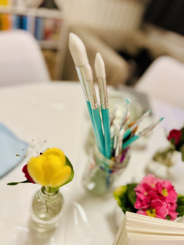 Yellow tulip and red rosebud in a small glass vase, colourful brushes behind