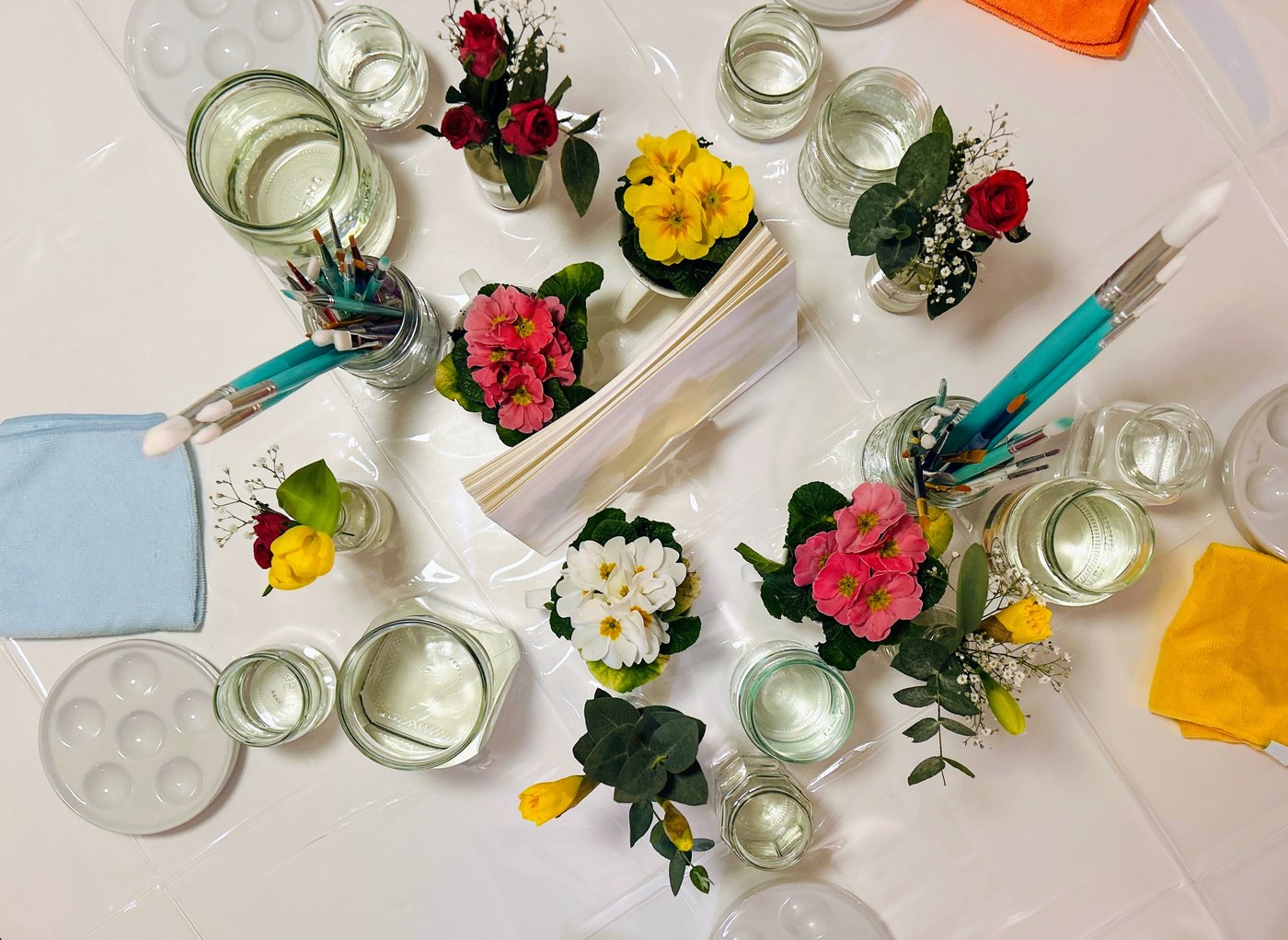 Bird's eye view of the painting table — primroses, roses, mason jars with brushes and paint palettes